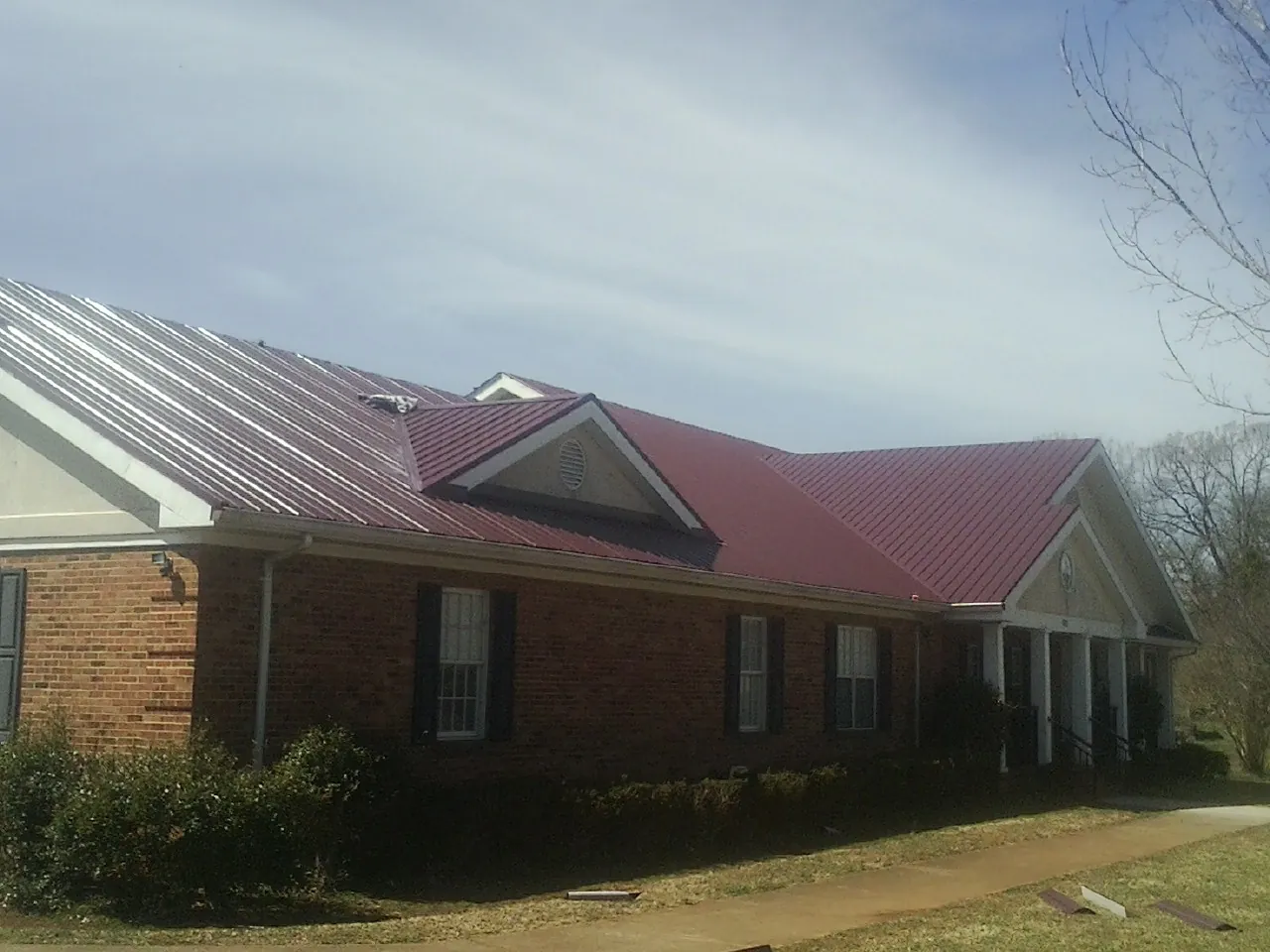 Red metal roof with gabled entries on a long brick building, from a Hail Damage Roof Repair job in Santa Paula