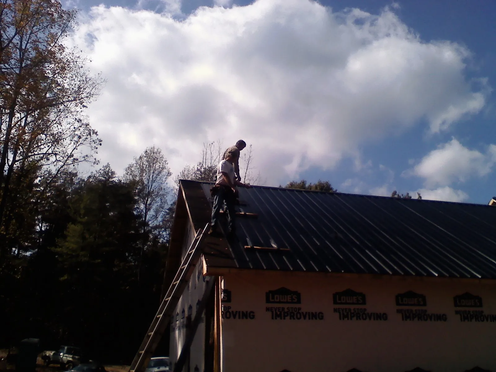 Roofer fastening dark metal panels high against a cloudy sky, from a Roof Inspection job in Santa Paula