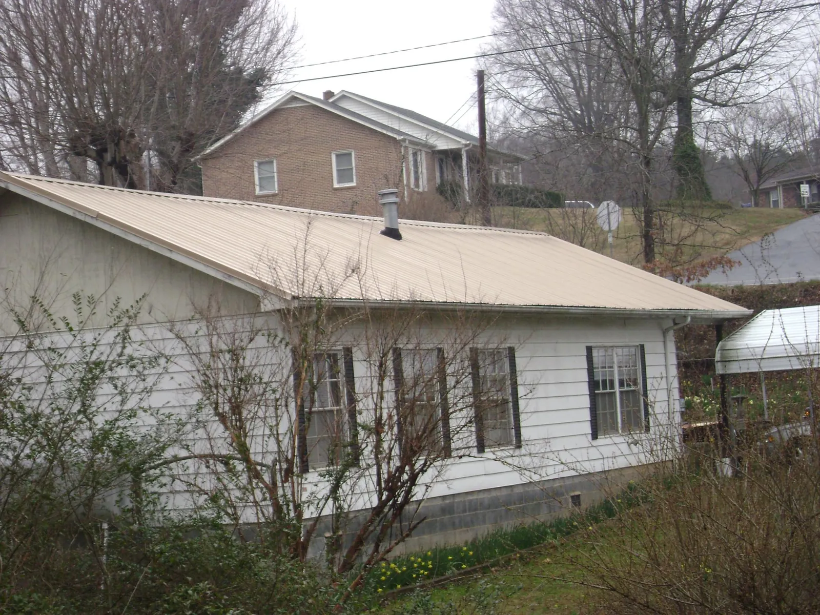 Tan metal roof on a white sided house set into a hillside — Commercial Roofing by Roofing Brothers in Santa Paula