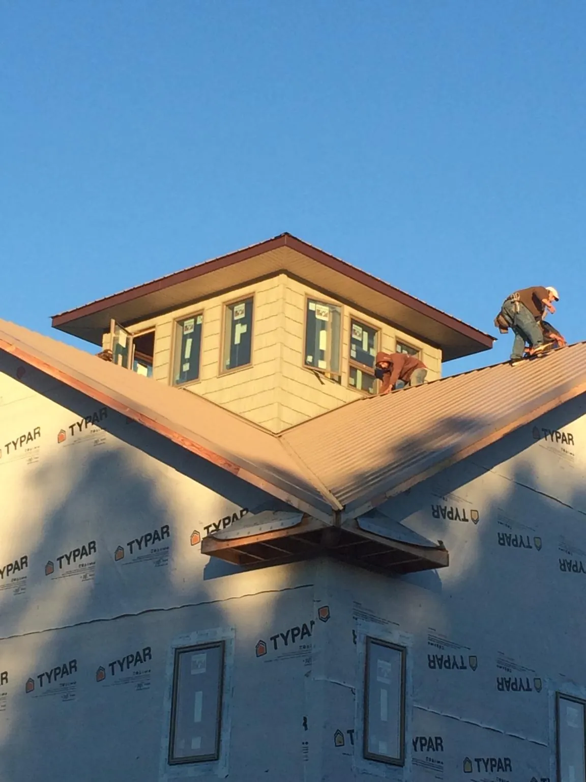 Roofers working around a rooftop cupola on a new metal roof at sunset — Roof Waterproofing in Santa Paula by Roofing Brothers